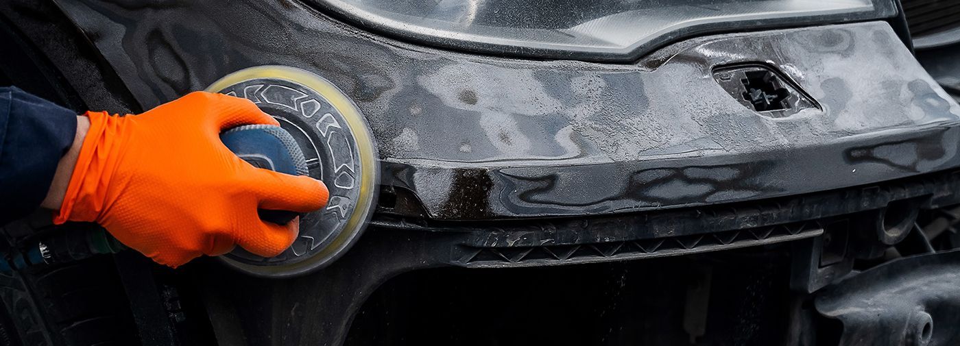 A gloved hand polishing a car's black bumper with a buffing tool.