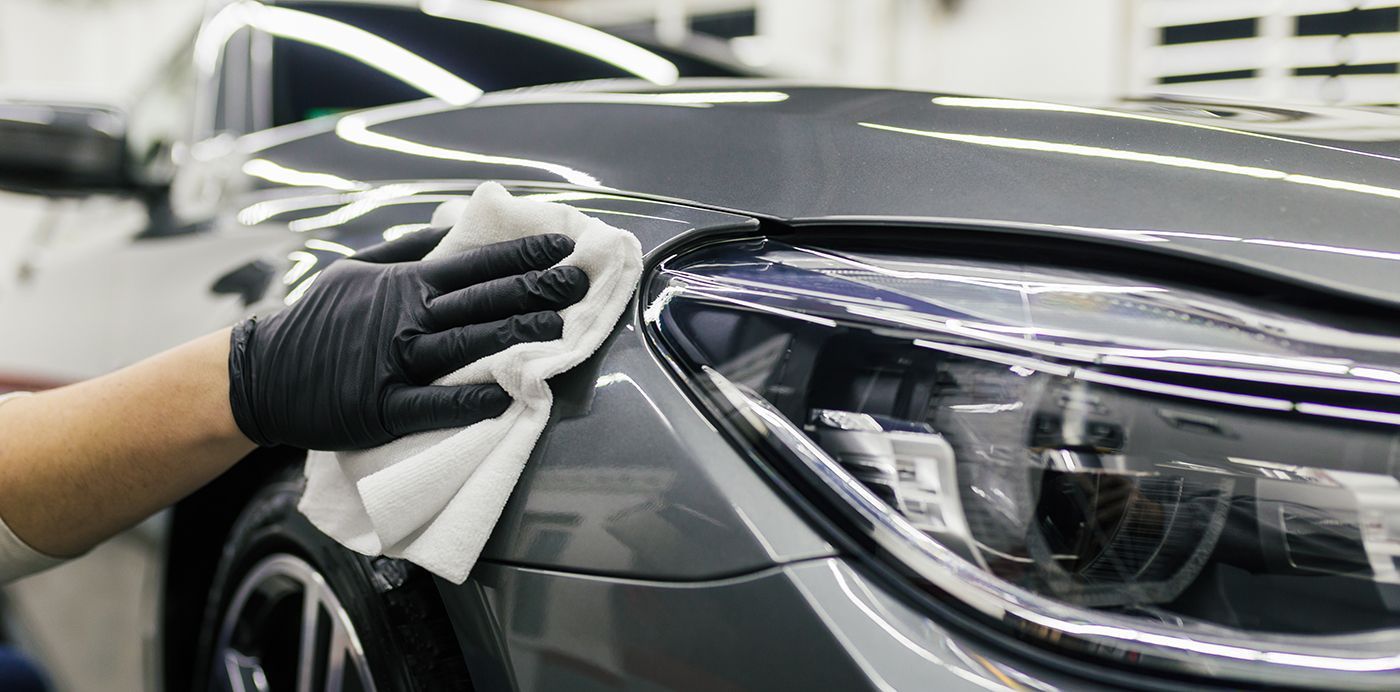 A person wearing a black glove wiping a gray car with a white cloth.