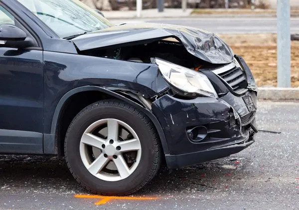 Front of a dark blue car with severe front-end damage after a collision on a wet road.