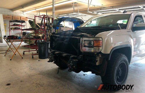 A white truck with the hood up is sitting in a garage.