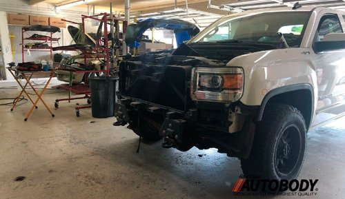 A white truck with the hood up is sitting in a garage.