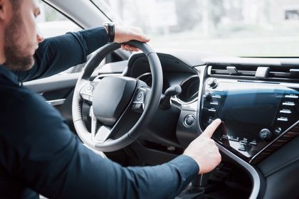Conducente che utilizza il touchscreen del cruscotto dell'auto tenendo il volante