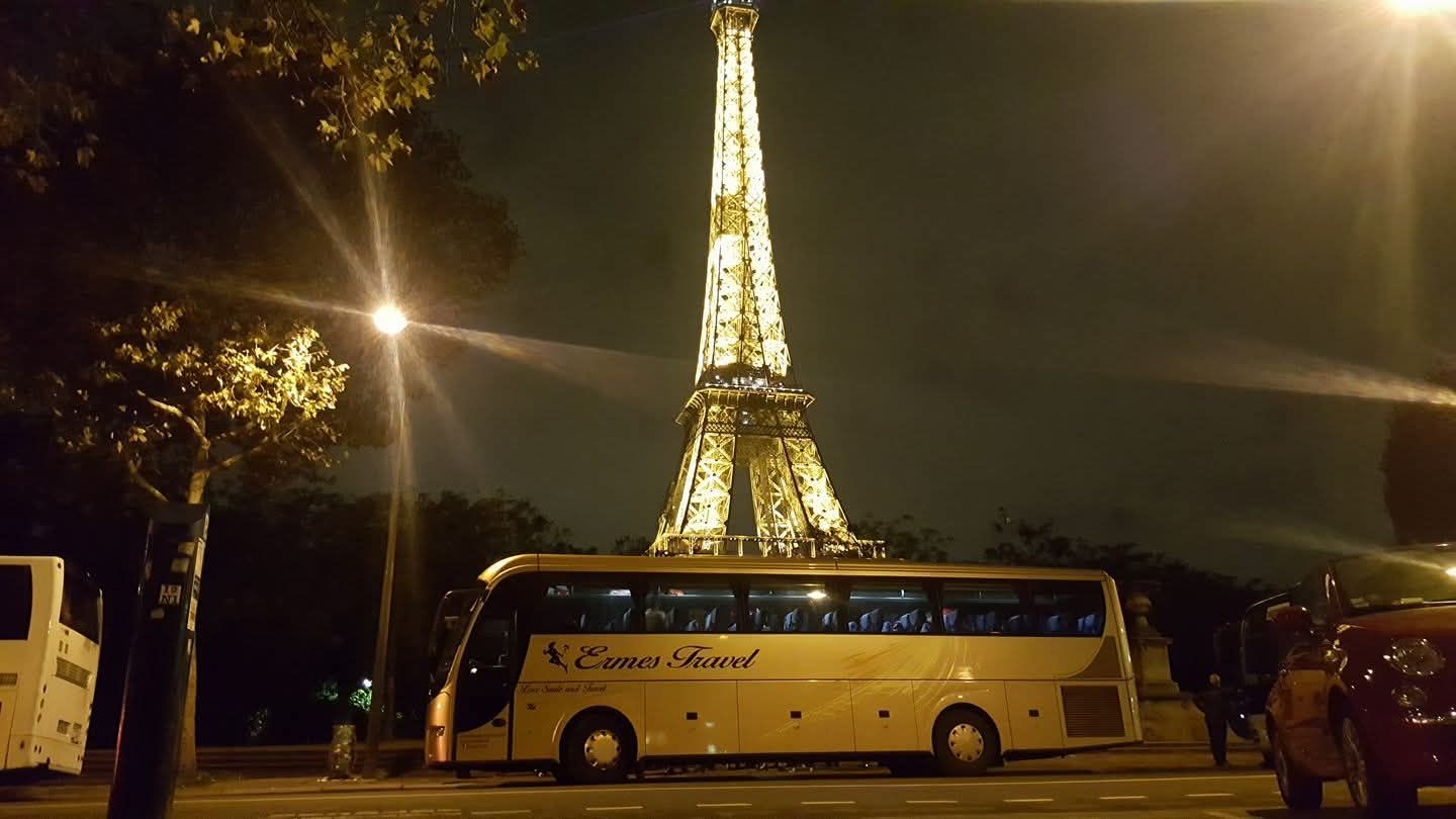 Autobus blu parcheggiati lungo la strada, con due persone in piedi accanto al bus più vicino sotto un cielo sereno.