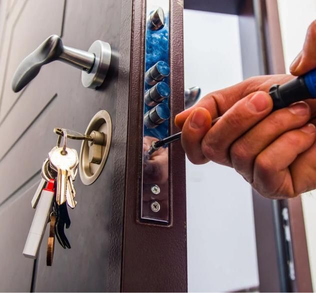 A person uses a screwdriver to adjust the locking mechanism on the edge of a brown metal door with keys in the keyhole.