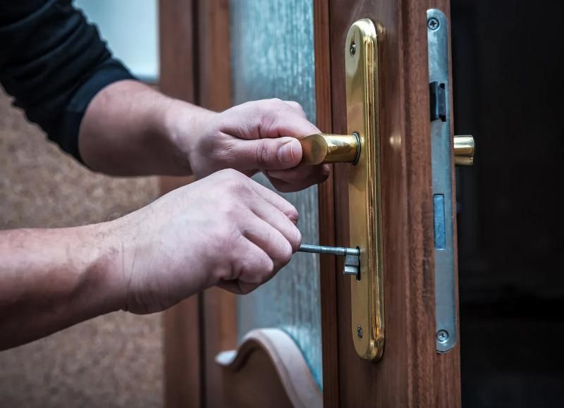 Hands inserting a key into a gold-toned door lock handle on a wooden door.