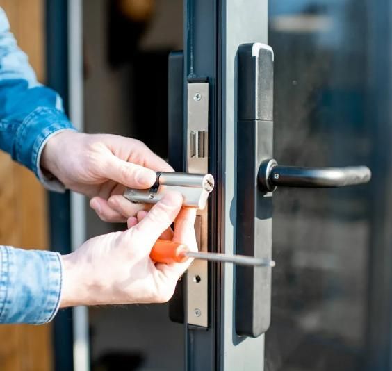 A person installing a metal euro profile cylinder lock into a black door handle assembly with a screwdriver.