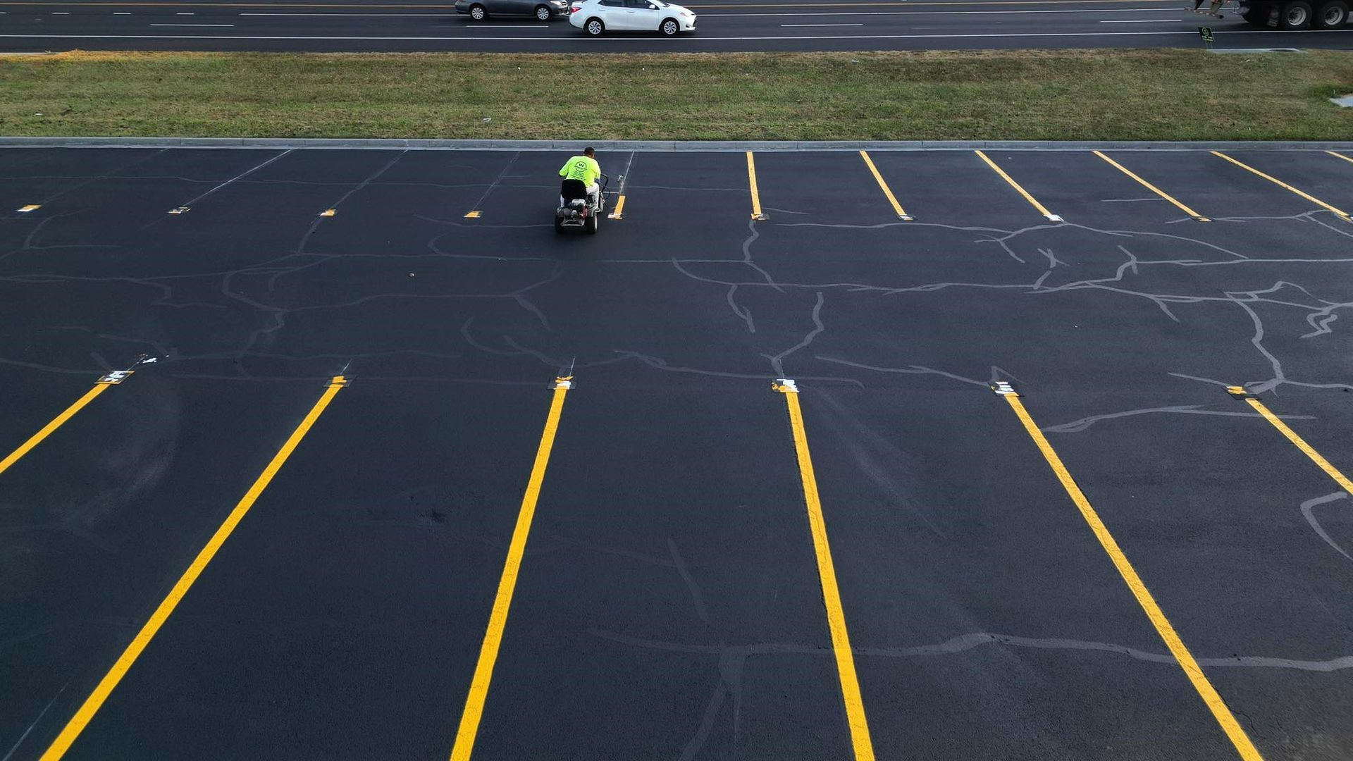 Image of a person painting the yellow lines of a parking lot space.
