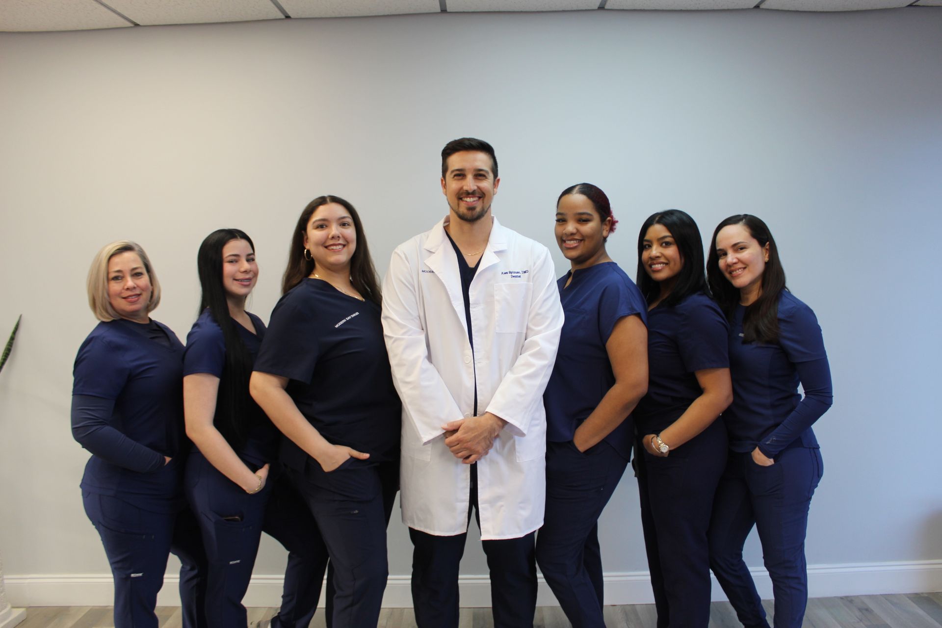 Group of six medical professionals in navy scrubs and a white coat standing together in a clinic hallway