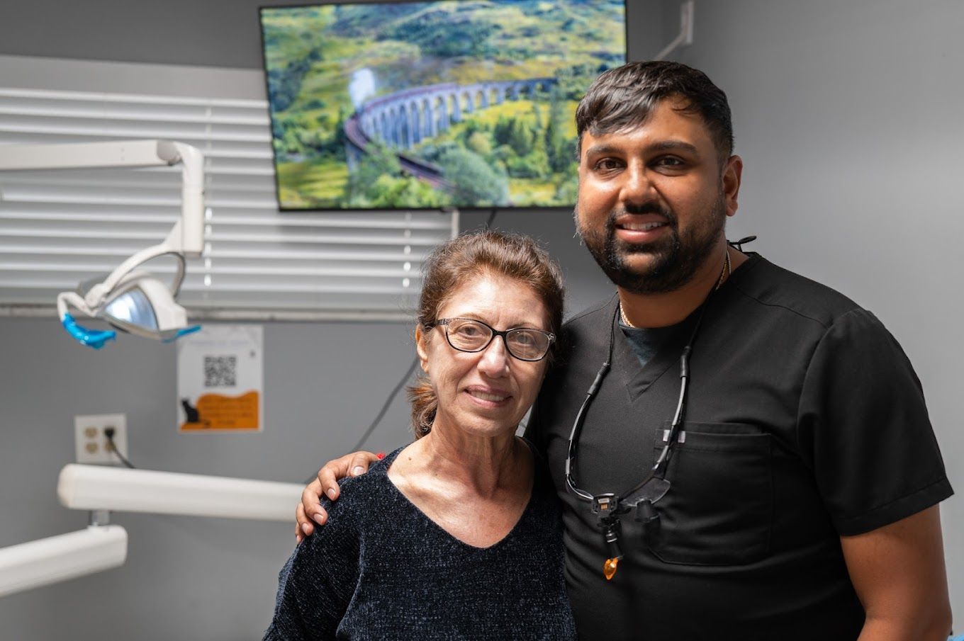 Dentist with patient in dental office; smiling, posed next to each other.