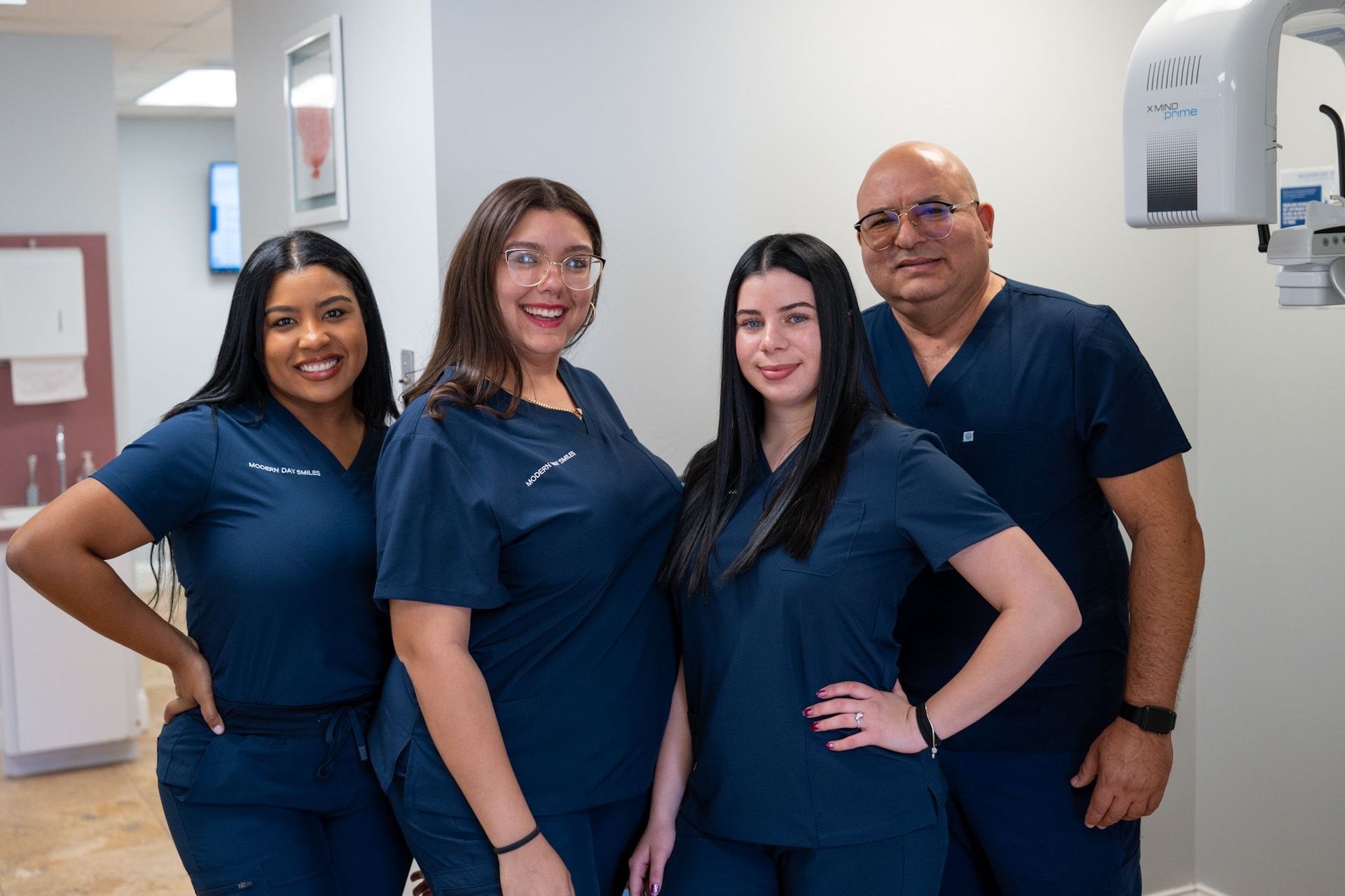 Four dental professionals in blue scrubs pose in an office, smiling.