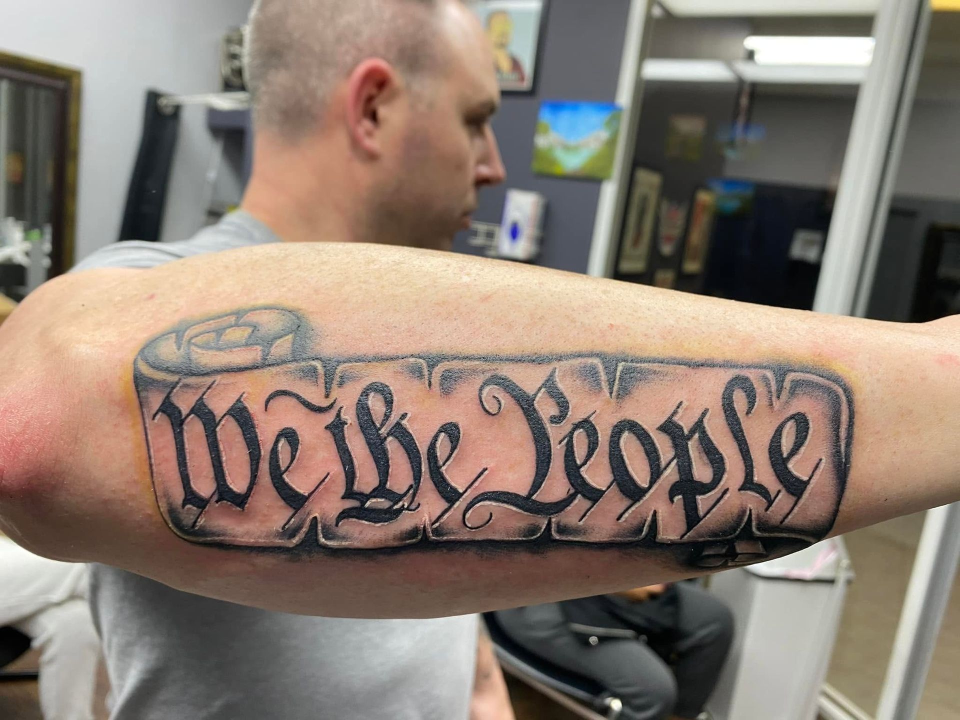 Tattoo by Eric Estrada at The Widow's Son Tattoo Co. in Gilbertsville, PA — We the People lettering on a banner across a forearm