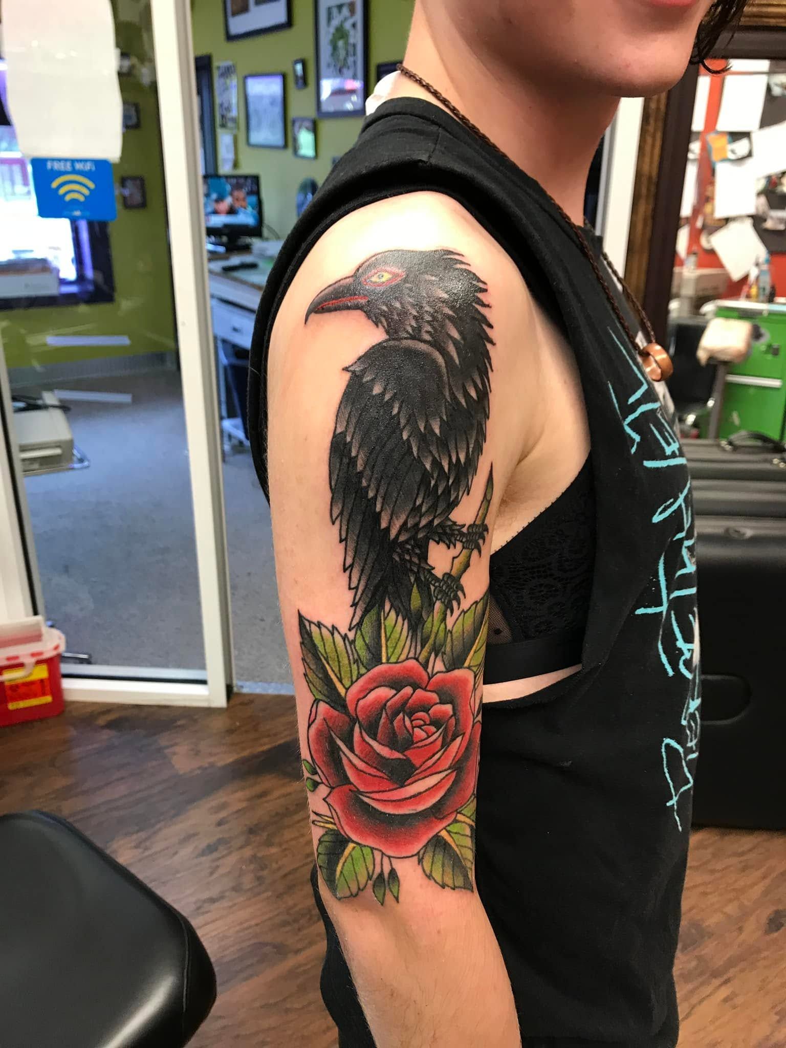 Tattoo by Eric Estrada at The Widow's Son Tattoo Co. in Gilbertsville, PA — a raven and a red rose on an upper arm
