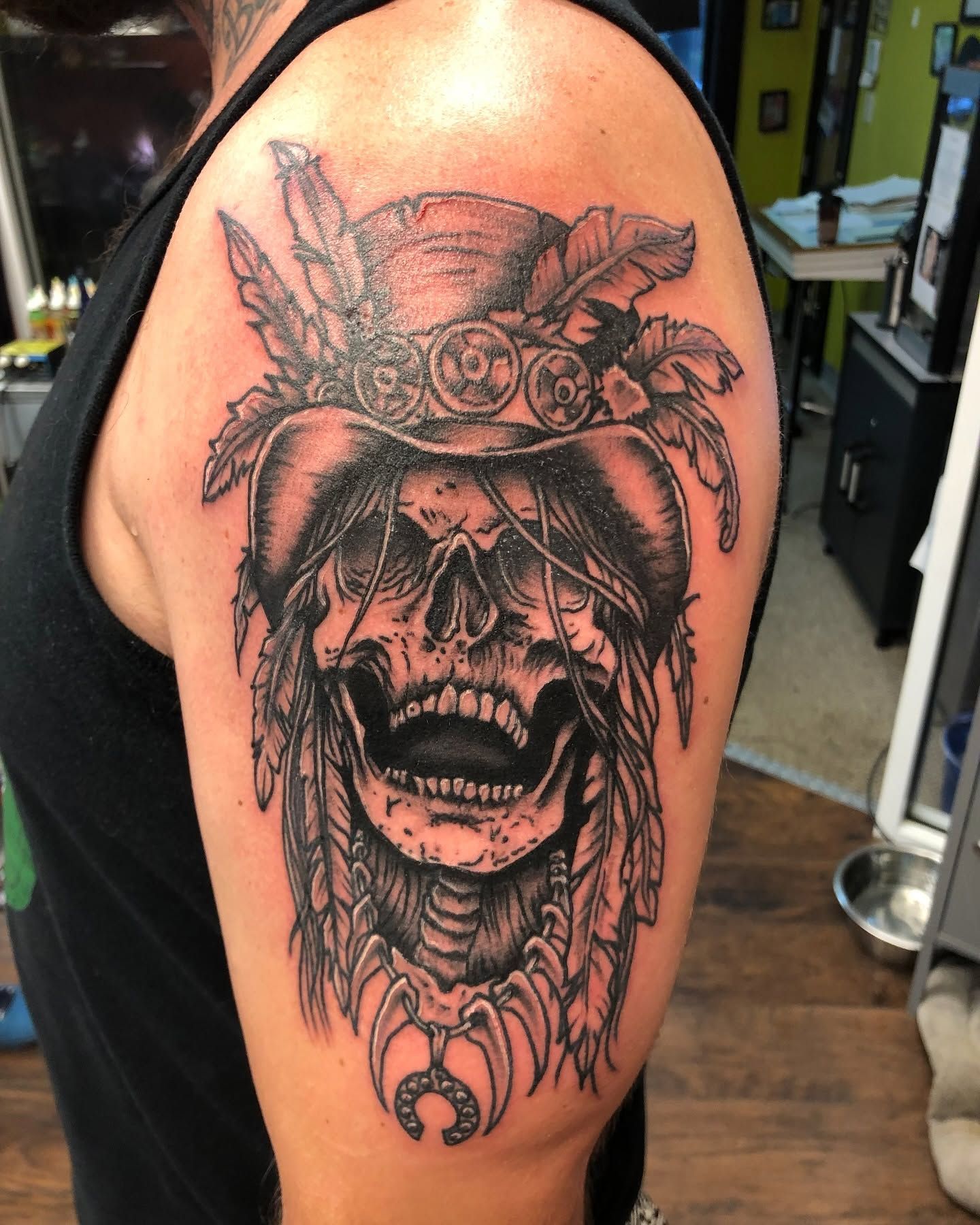 Tattoo by Eric Estrada at The Widow's Son Tattoo Co. in Gilbertsville, PA — a black and grey skull in a feathered headdress on an upper arm