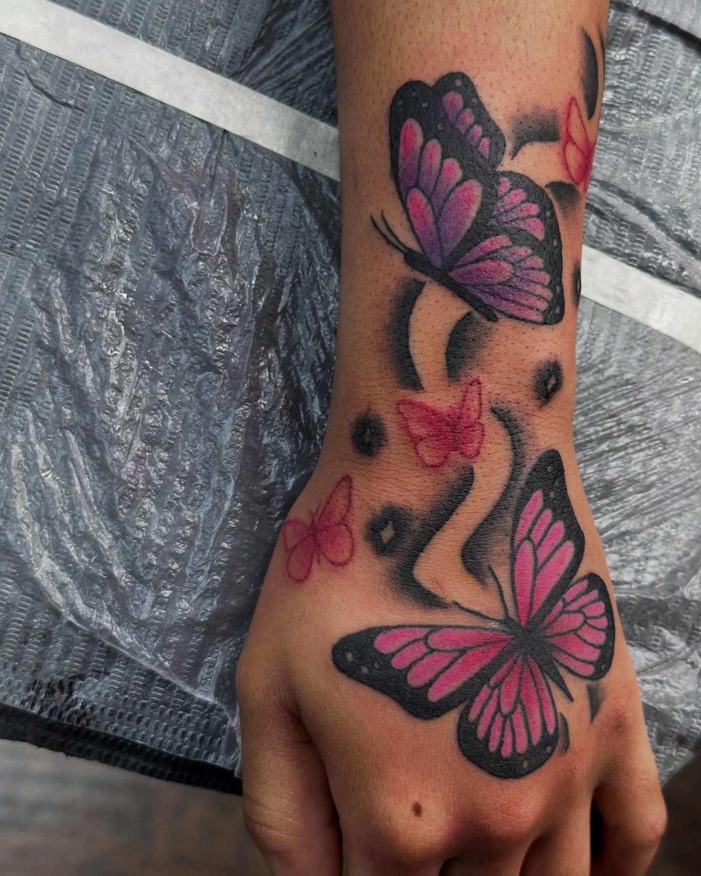 Tattoo by Eric Estrada at The Widow's Son Tattoo Co. in Gilbertsville, PA — butterflies and flowers in pink and purple across a hand