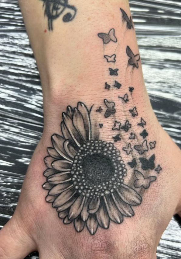 Tattoo by Tom Kelly at The Widow's Son Tattoo Co. in Gilbertsville, PA — a sunflower and butterflies across a hand