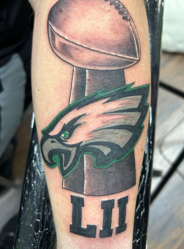 Tattoo by Tom Kelly at The Widow's Son Tattoo Co. in Gilbertsville, PA — a commemorative football piece on an arm