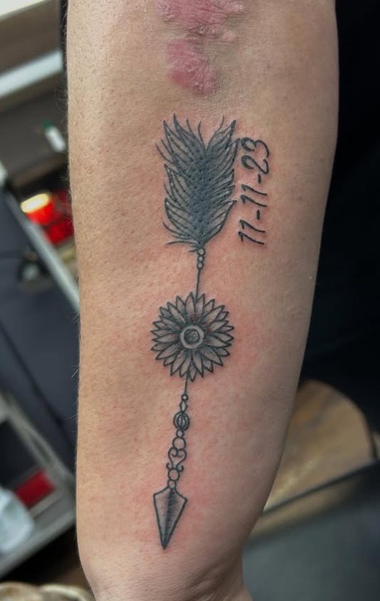 Tattoo by Tom Kelly at The Widow's Son Tattoo Co. in Gilbertsville, PA — a feather, a sunflower and a date in black and grey