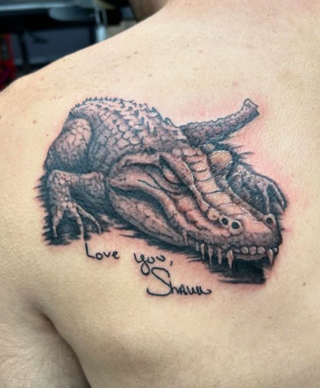 Tattoo by Tom Kelly at The Widow's Son Tattoo Co. in Gilbertsville, PA — a black and grey crocodile with lettering