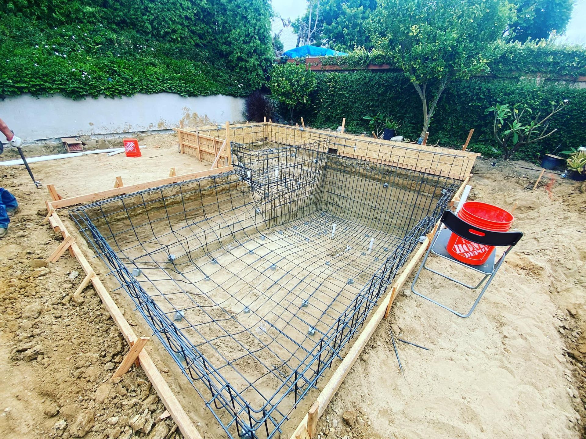 Pool under construction with wooden forms, rebar grid, and surrounding dirt.