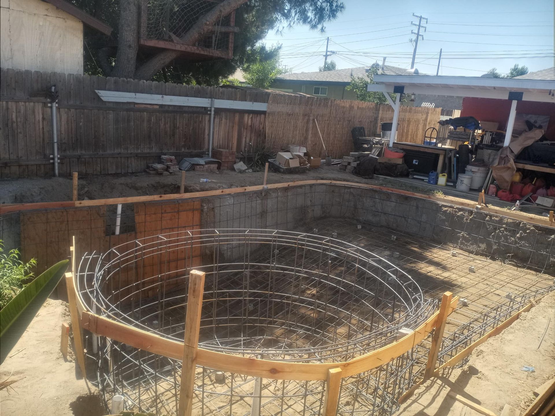 Construction site with a circular pool form and rebar framework in a yard.
