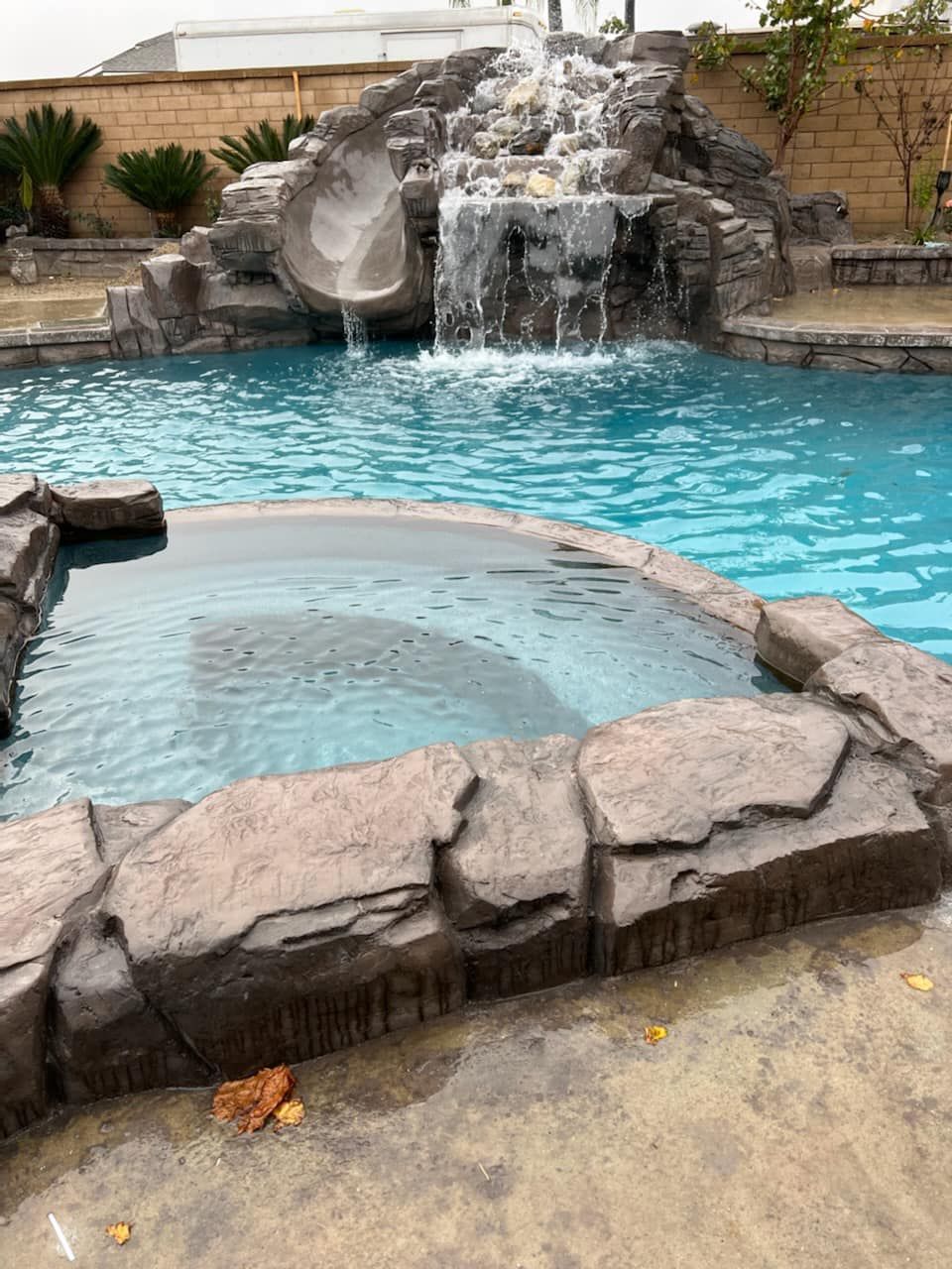 Swimming pool with a rock waterfall, slide, and a hot tub.