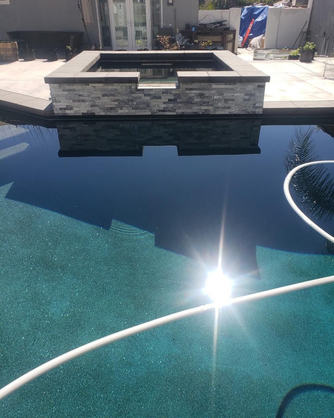 Swimming pool with dark water, stone wall feature, bright sunlight reflection.