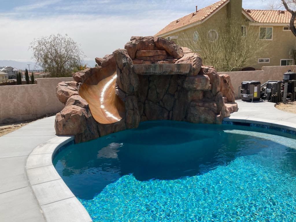 Swimming pool with blue water and concrete patio, bordered by a black fence.