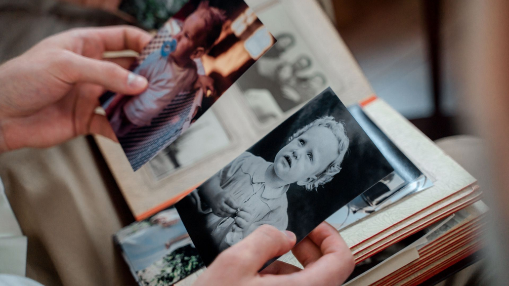 Hands holding printed family photos, including a black-and-white portrait, over a stack of snapshots