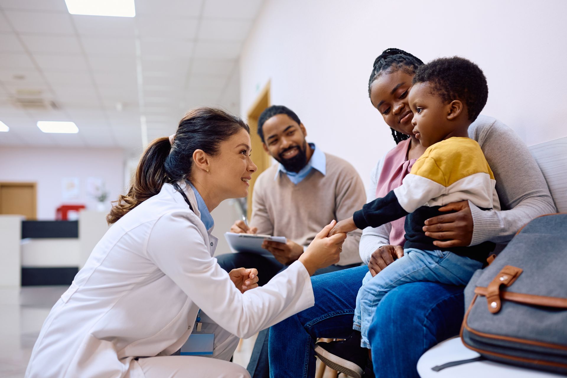 Family doctor greeting a young child during a checkup while his parents look on.
