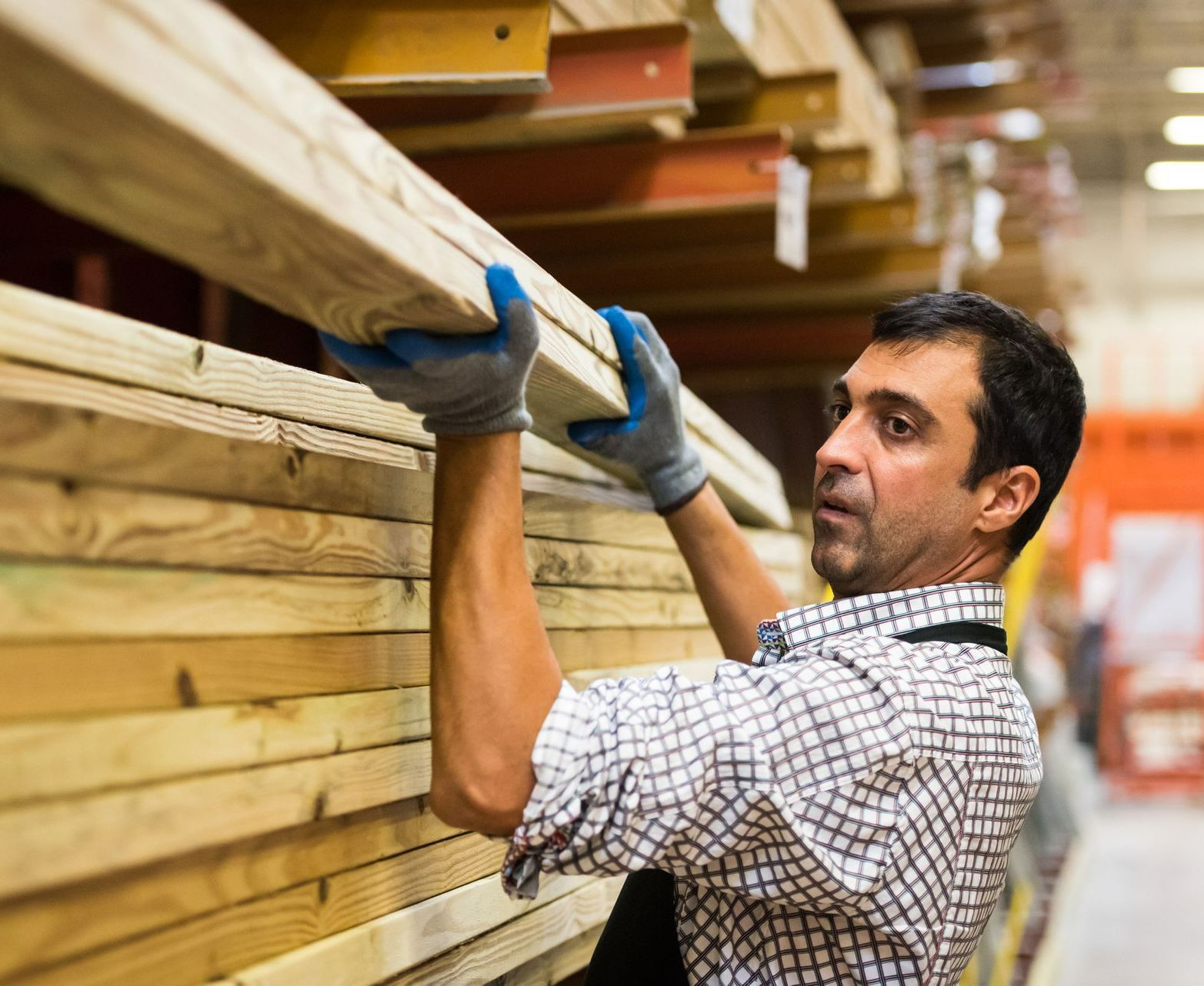 A man is holding a piece of wood in a warehouse.