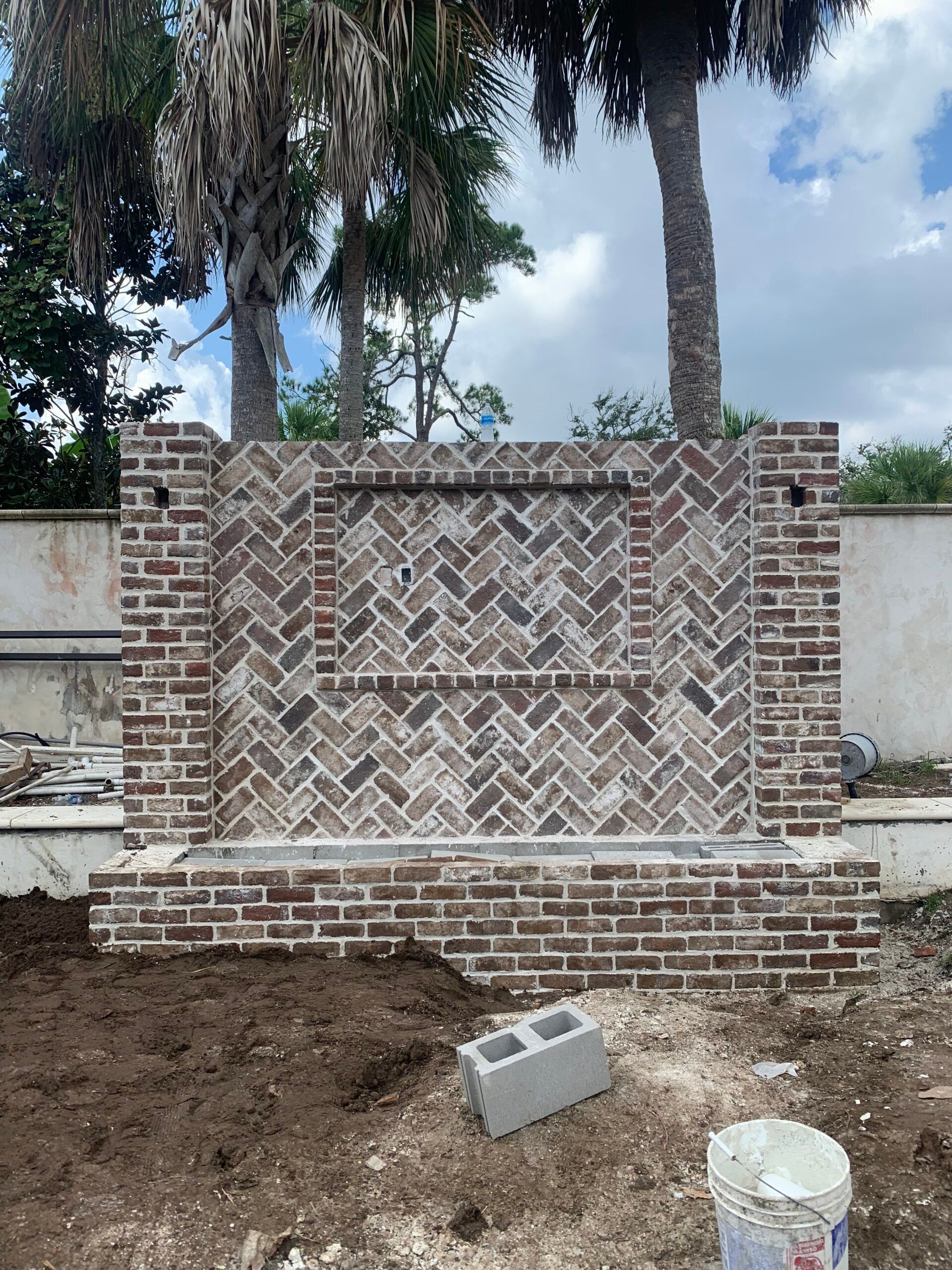 A brick wall is being built in a yard with palm trees in the background