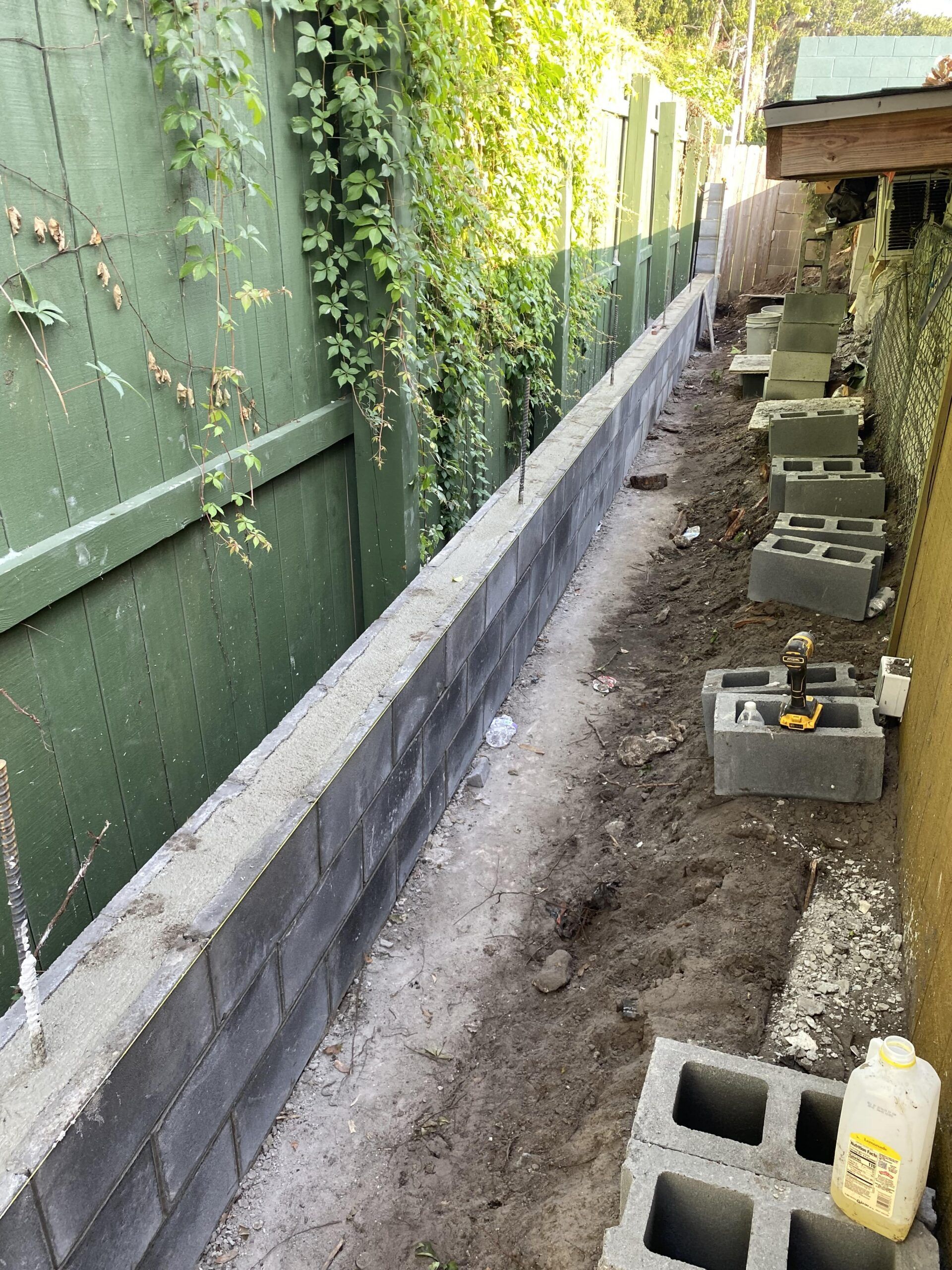A brick wall is being built next to a green fence.