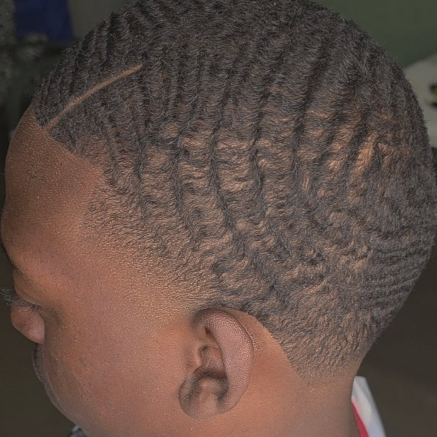 Close-up of a child’s braided hairstyle with short tapered sides against a neutral background