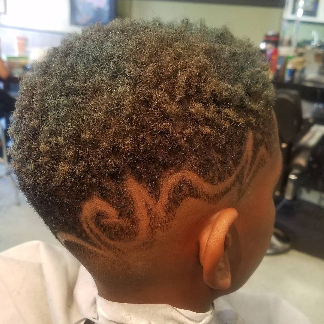 Short curly haircut with shaved wave design on the side, shown in a barbershop.