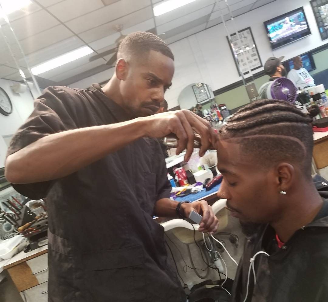 Barber trimming a client's braided hair in a busy salon
