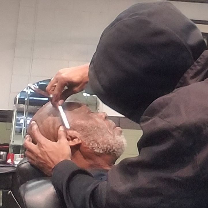 Barber trimming an older man’s hair with clippers in a salon chair