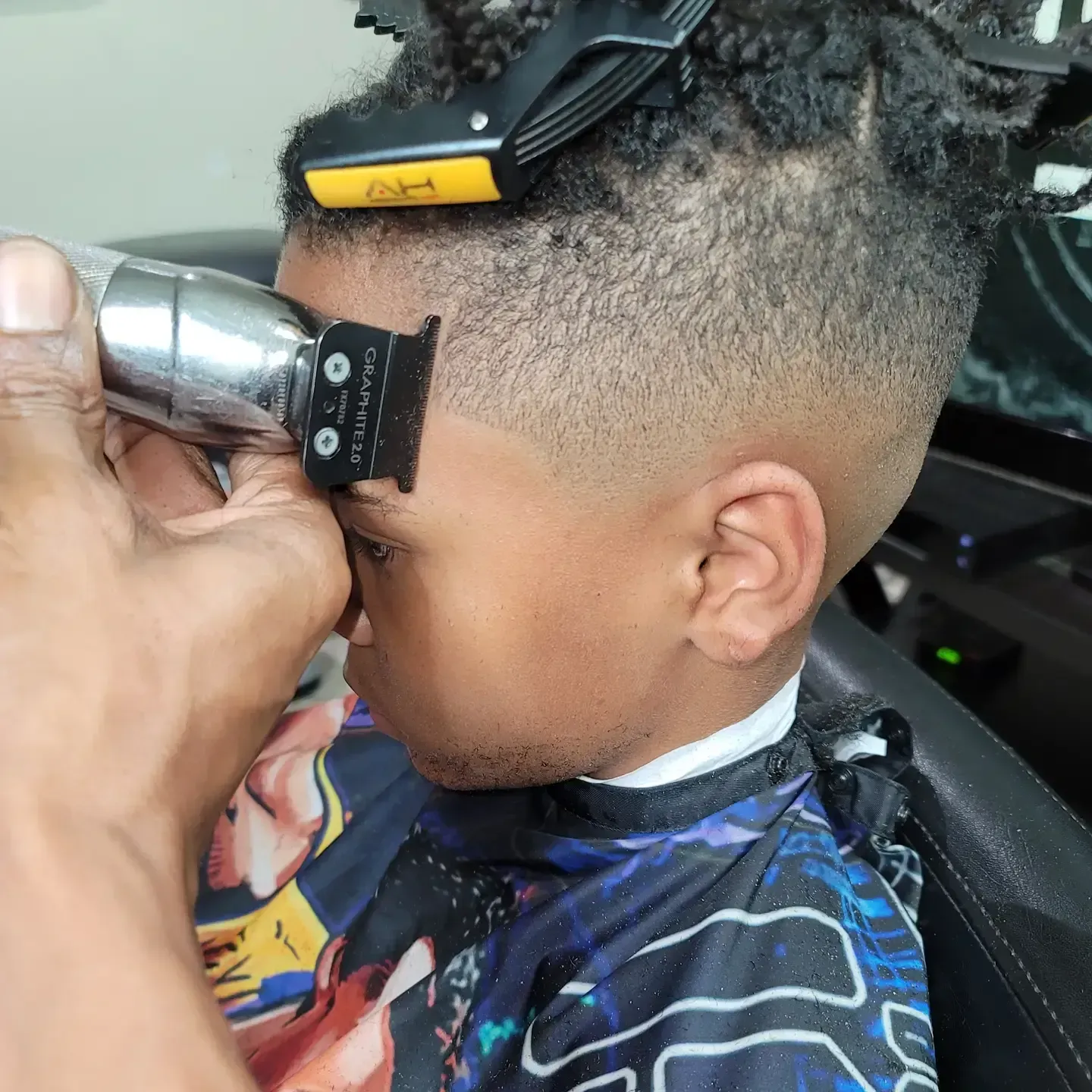 Child getting a haircut with electric clippers in a barber chair