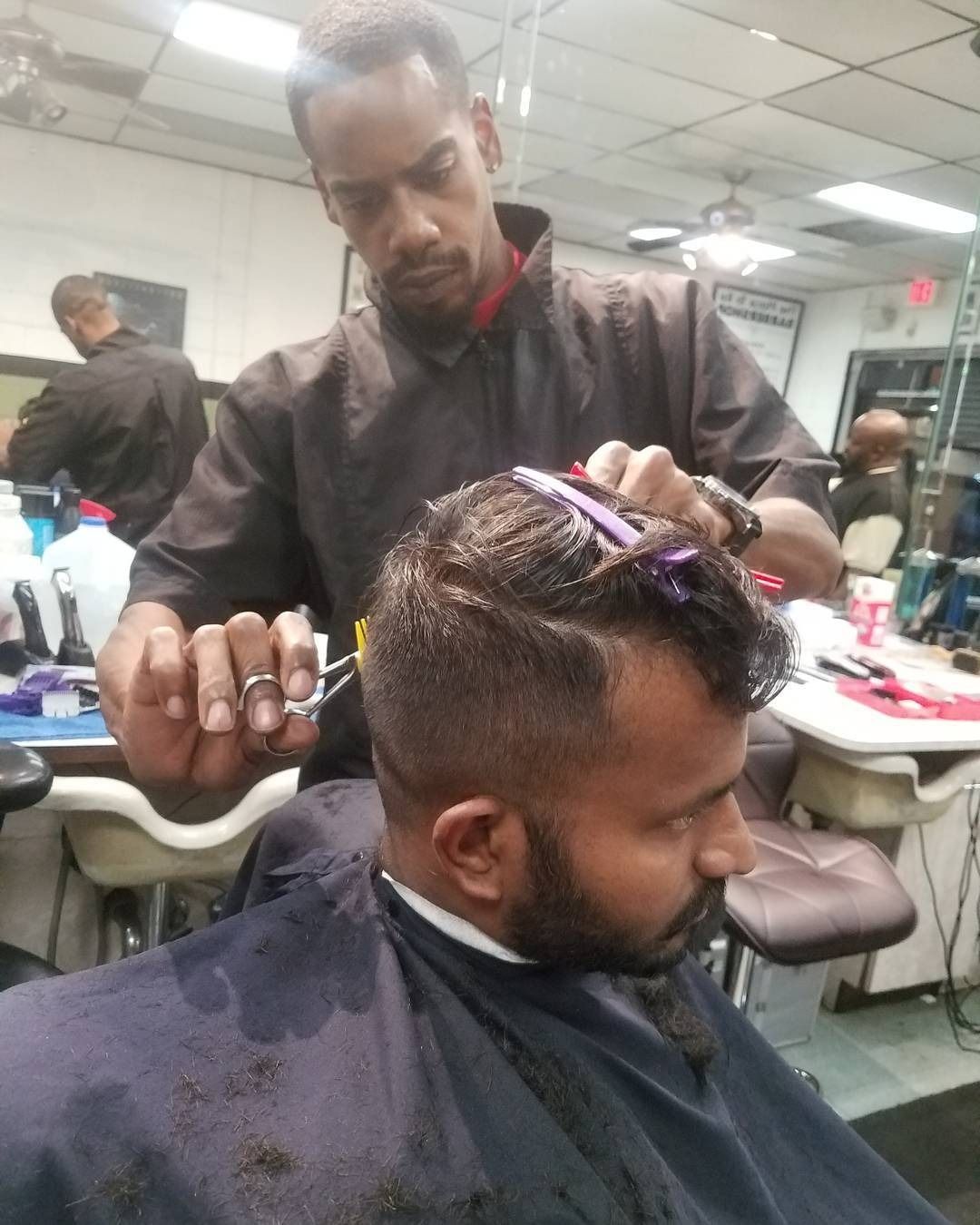 Barber trimming a man’s hair in a salon, with clippers and comb visible.