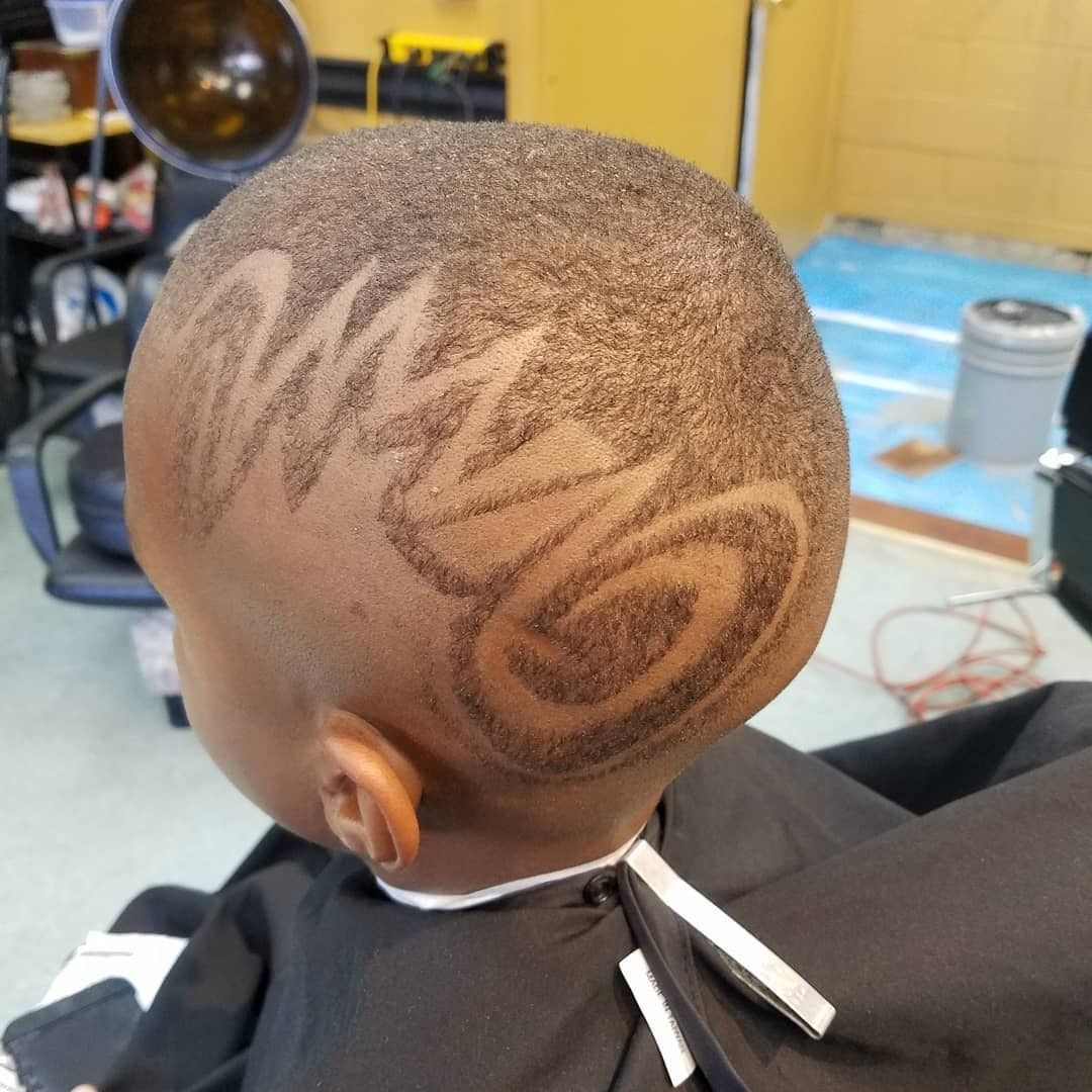 Close-up of a child’s shaved haircut with zigzag and swirl designs at a barbershop.