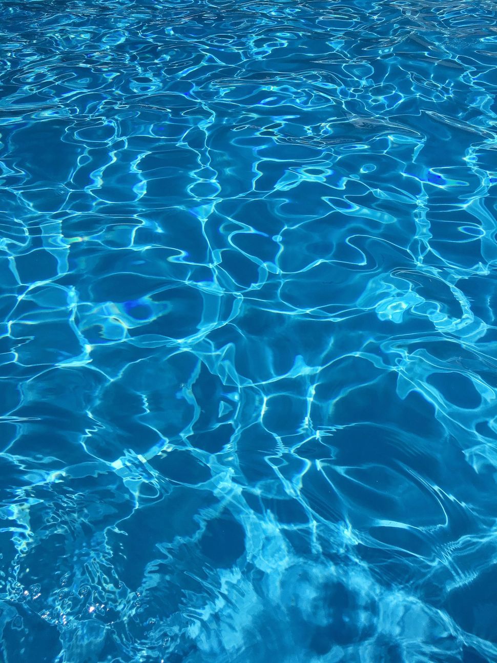 Sunlit blue swimming pool water with rippling reflections