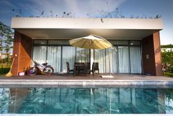 Modern villa patio with pool, lounge chairs, umbrella, and glass doors reflected in the water