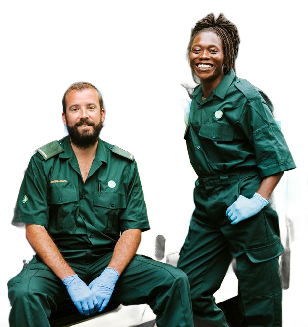 Two paramedics in green uniforms, one seated and one standing, both wearing blue gloves and smiling.