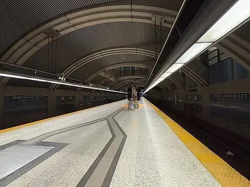 Empty subway platform with arched ceiling, yellow edge strip, and a few people in the distance