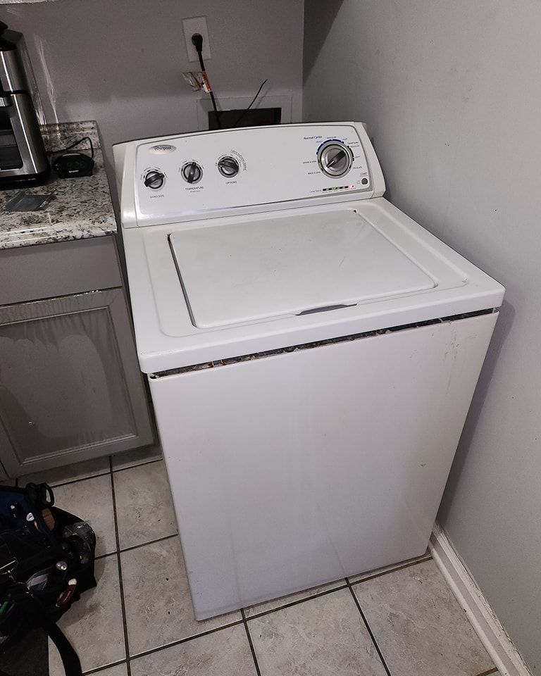 A white washing machine is sitting in a laundry room next to a counter.