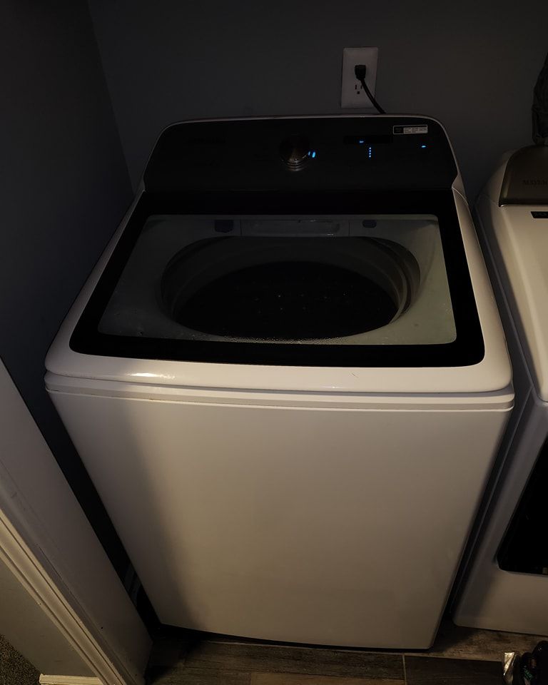 A white washing machine is sitting in a laundry room next to a stove.