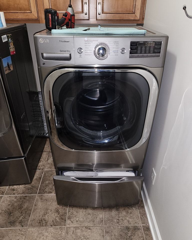 A stainless steel washing machine is sitting on a tiled floor in a laundry room.