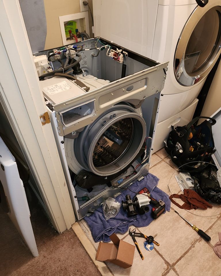 A broken washing machine is sitting on the floor in a laundry room.