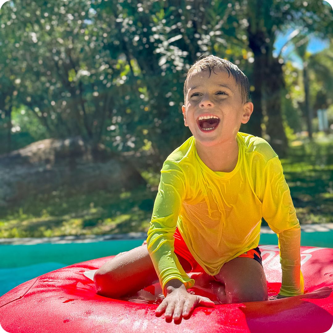 Menino sorrindo e se divertindo em uma boia vermelha na piscina cercada por natureza no resort Enotel Porto de Galinhas, destacando a viagem em família no mês das crianças em outubro.