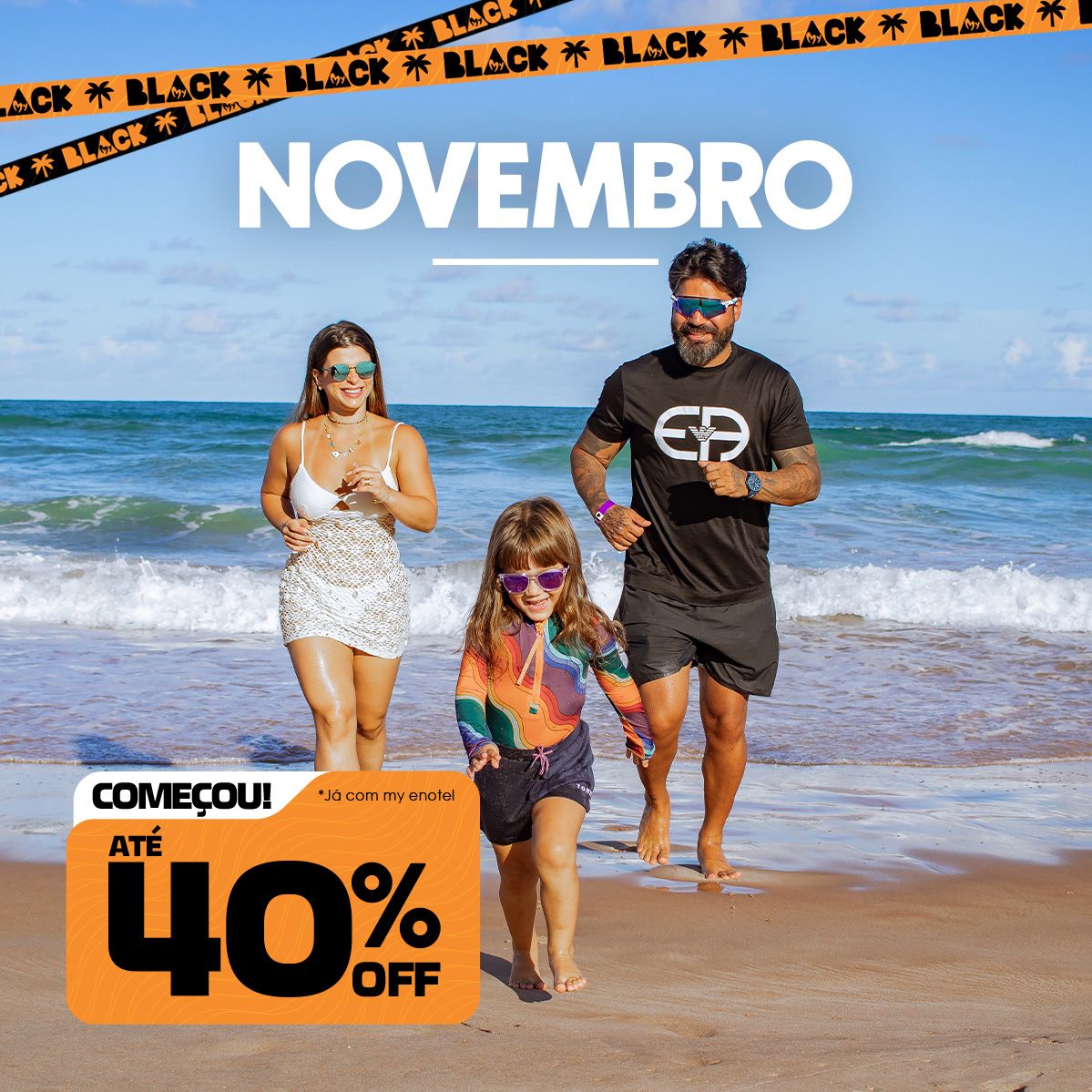 Família sorridente caminhando na praia do Enotel em um dia ensolarado, com o texto Novembro em destaque e faixas da campanha My Black no topo. No canto inferior esquerdo, há um selo da promoção com a frase 