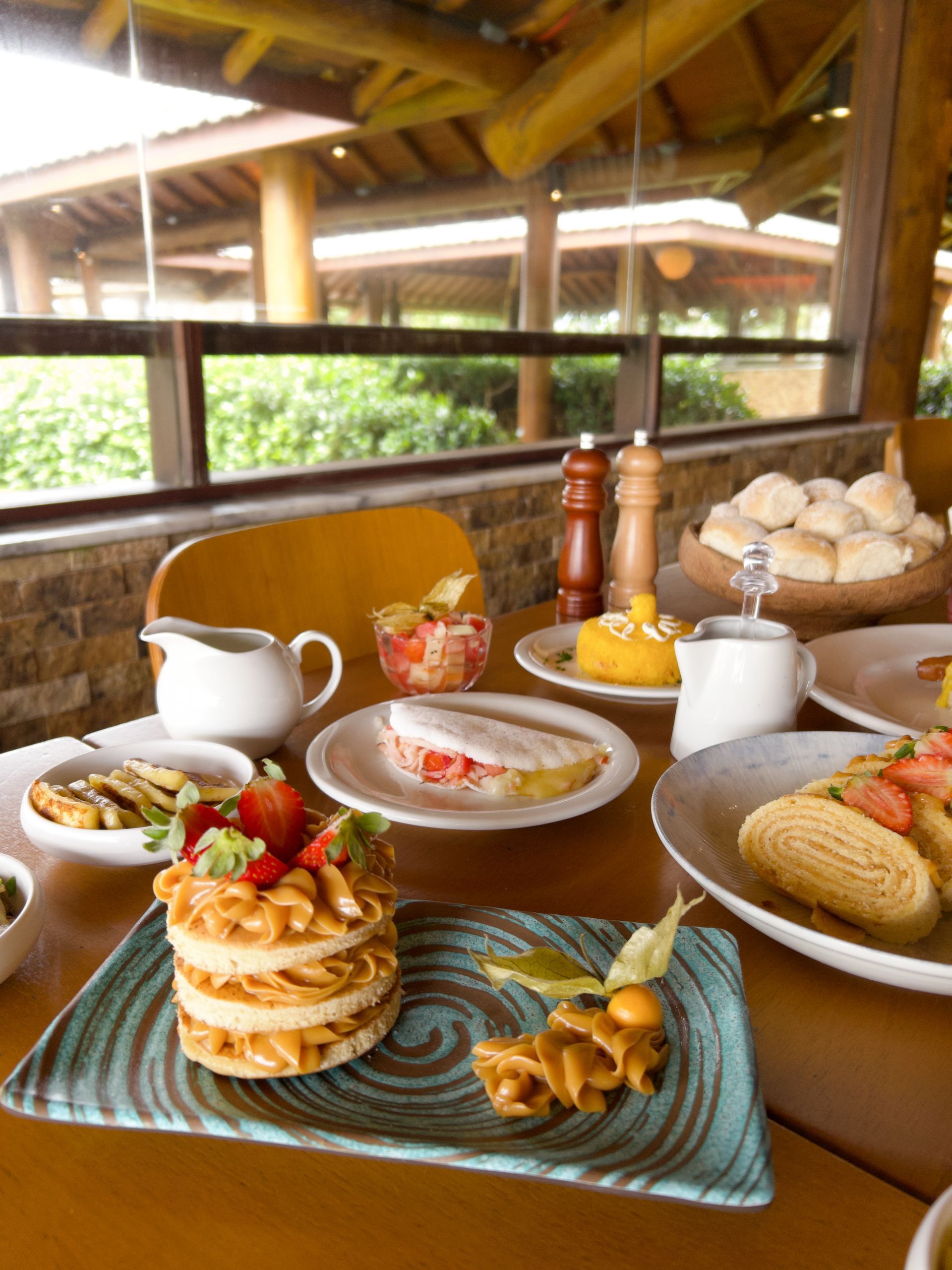 Café da manhã com bolo de rolo, tapioca e frutas no resort Enotel. Mesa farta em ambiente rústico com vista para o jardim